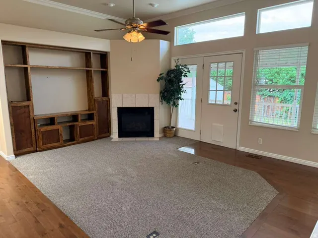 Living area featuring a corner fireplace with tile surround, built-in entertainment center with wood-finish shelving, and a ceiling fan with integrated lighting