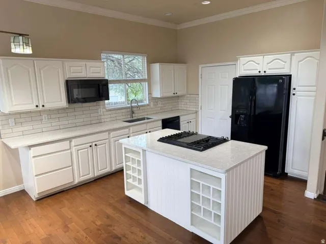 Kitchen featuring white cabinetry, subway tile backsplash, light-toned countertops, a central island with integrated storage, and wood-finish flooring