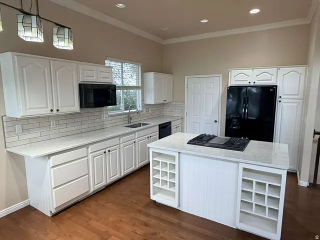 Kitchen featuring an island with built-in wine storage, white cabinetry, integrated black appliances, light-colored countertops, and wood-finish flooring