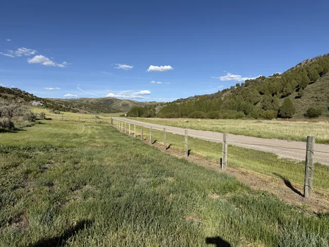 Expansive open landscape featuring a gravel road, wire fencing, and distant hills with scattered trees