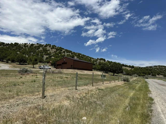 Brown metal-sided building with two garage doors, situated on a sloped hillside lot with scattered trees and natural vegetation