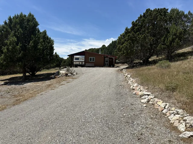Gravel driveway with natural rock border leading to a brown-sided residence featuring a covered porch