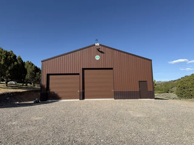 Brown metal building featuring two large roll-up doors, a single entry door, and a gravel parking area