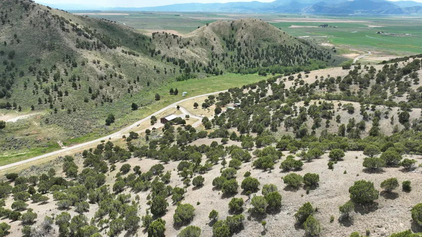 Expansive rural property featuring rolling hills, mature trees, a visible structure, and distant mountain ranges