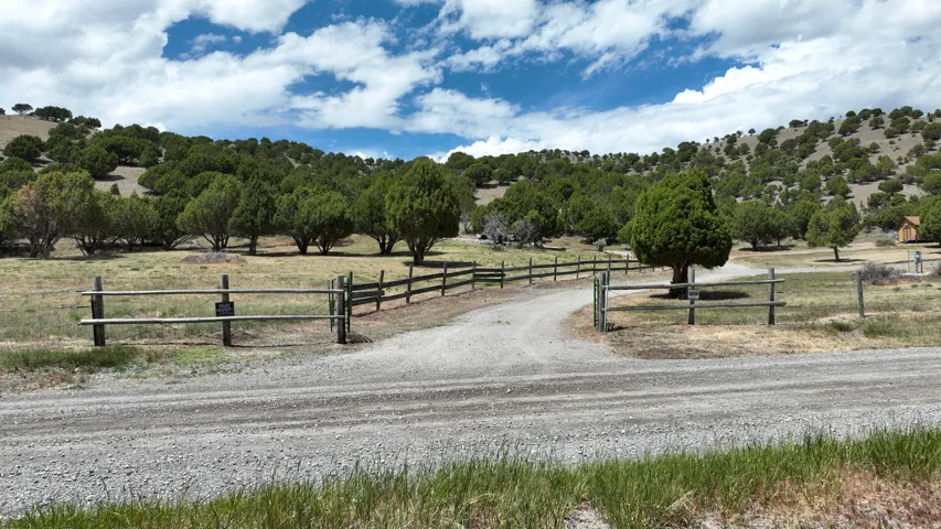 Expansive rural property featuring a gravel driveway and a rustic wooden fence