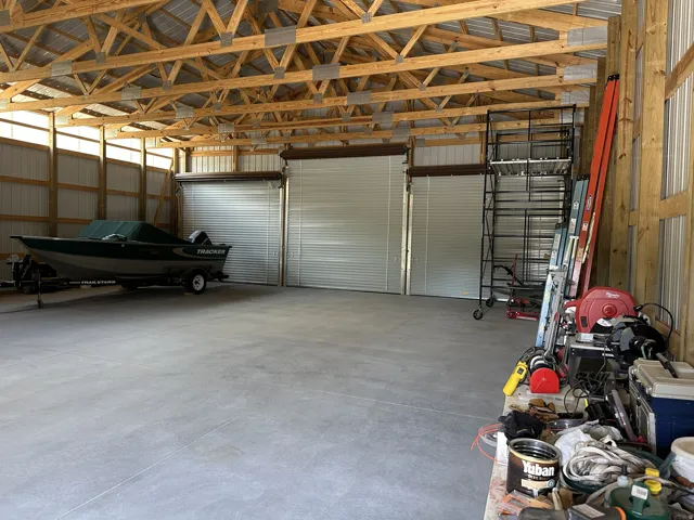 Spacious outbuilding featuring a concrete floor, exposed wood truss ceiling, and three roll-up doors for versatile access