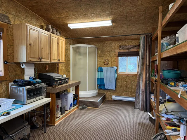 Room featuring wood-finish paneling, a compact stand-up shower, built-in wooden shelving, and upper cabinetry