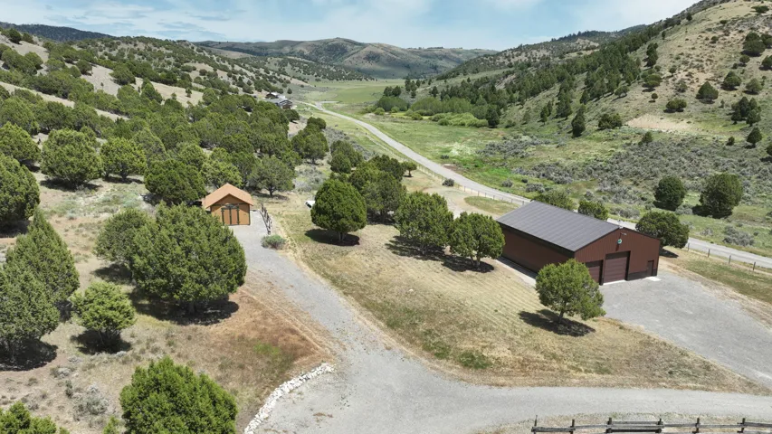Expansive property featuring a large brown metal-sided structure with two garage doors, a smaller wood-sided building with a gable roof, and a gravel driveway