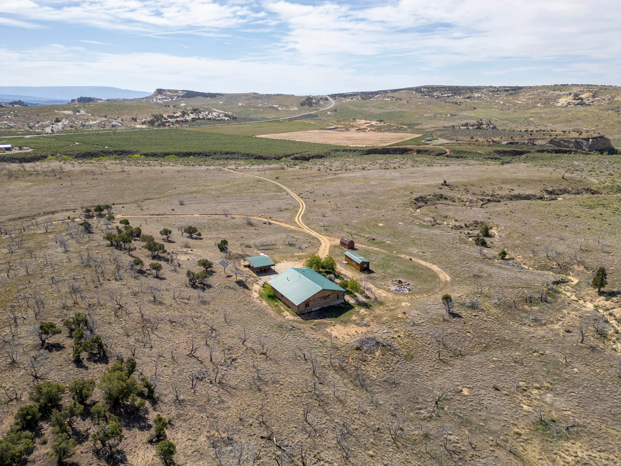 Expansive property featuring a central residence with a green metal roof, a dirt access road, and multiple outbuildings