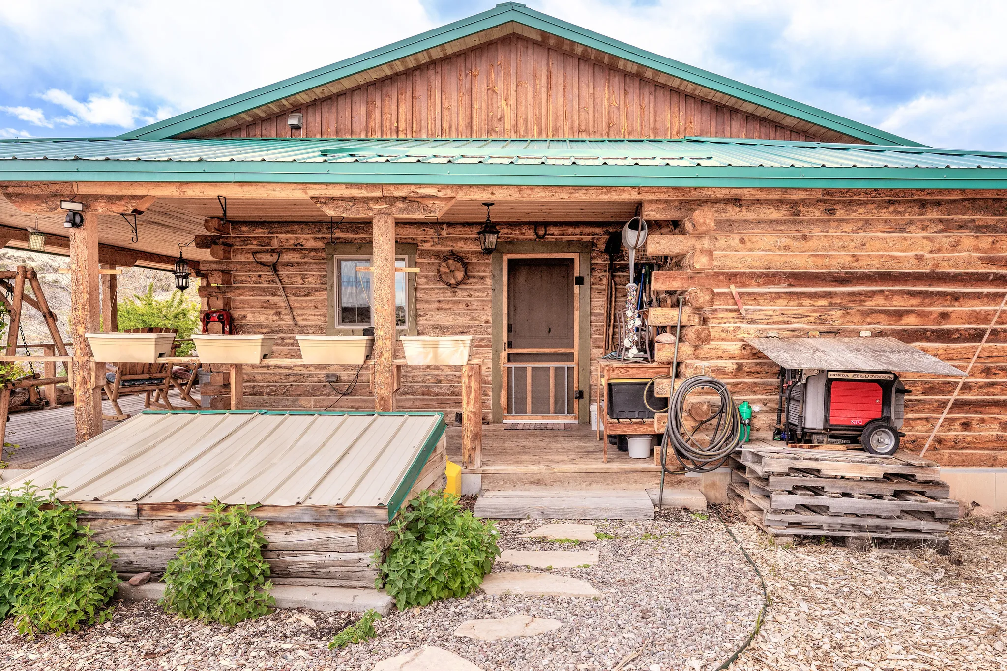 Rustic log cabin exterior featuring a green metal roof, a covered front porch with log posts, and a gravel pathway