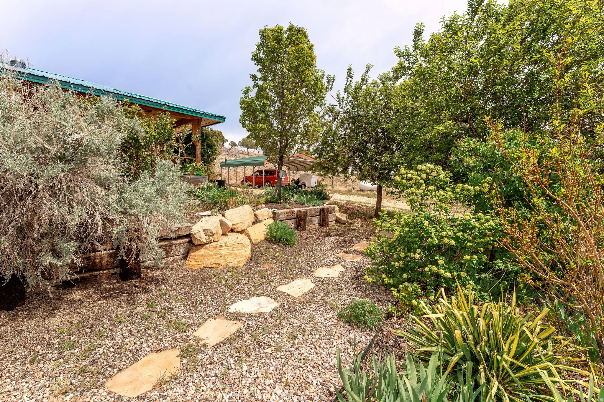 Natural stone paver pathway featuring a gravel bed and mature landscaping, with a visible portion of a residence featuring a green metal roof