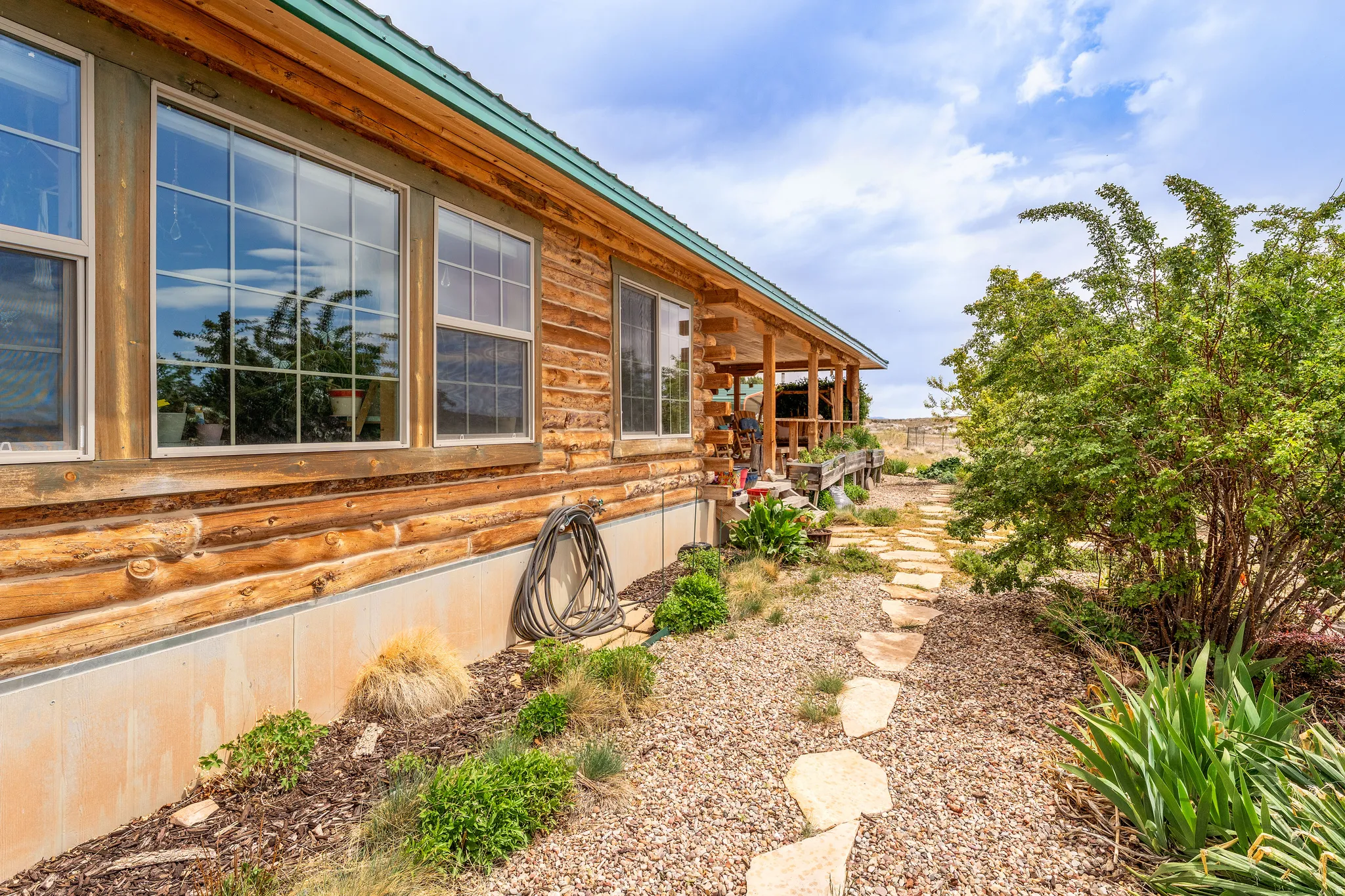 Wood-sided exterior featuring multiple windows with grids, a covered porch, a stone pathway, and a gravel landscape with mature plantings