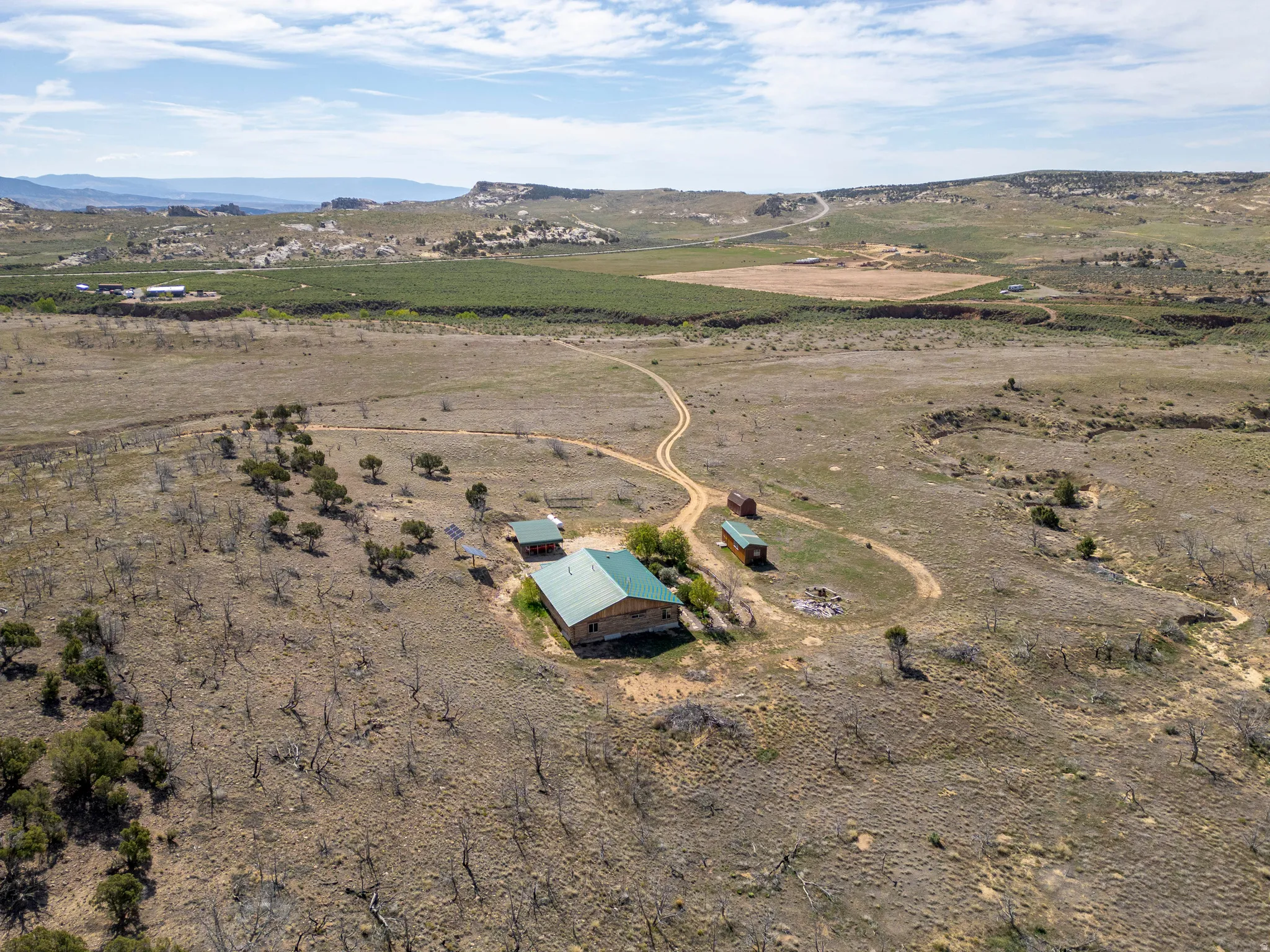 Expansive property featuring a central residence with a green metal roof, multiple outbuildings, and a meandering dirt road