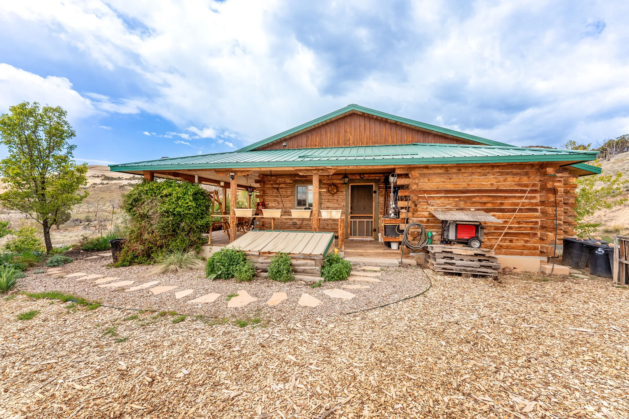 Log cabin exterior with a green metal roof, covered front porch, and a stone pathway