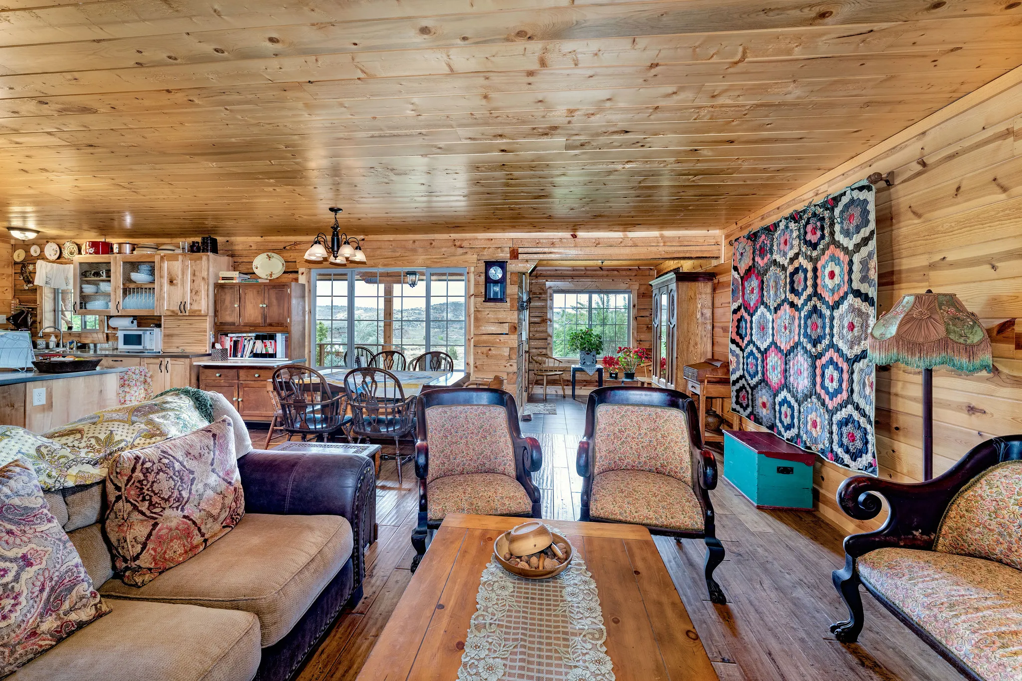 Spacious living area featuring extensive wood-finish paneling on walls and ceiling, wood-finish flooring, a built-in kitchen cabinetry with glass-front uppers, and large windows providing abundant natural light