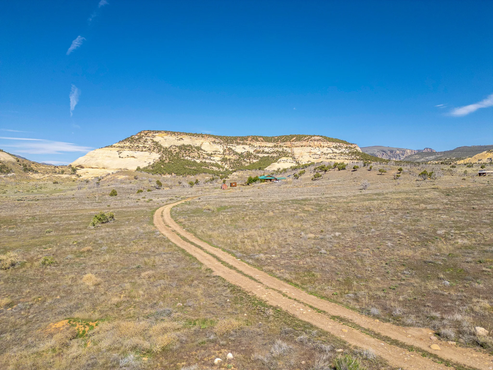 Expansive open land featuring a winding dirt road, distant structures, and a prominent mesa backdrop