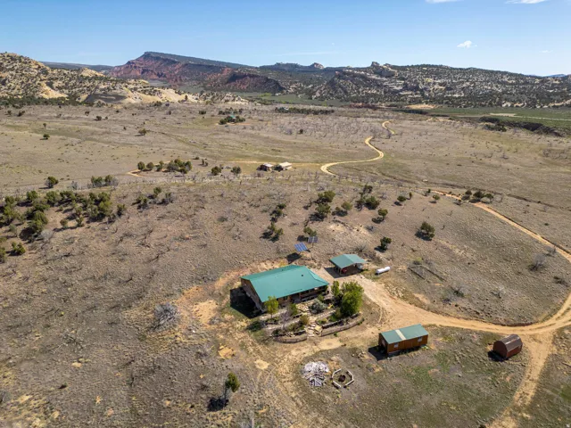 Expansive property featuring a main residence with a green metal roof, multiple outbuildings, and a meandering dirt road