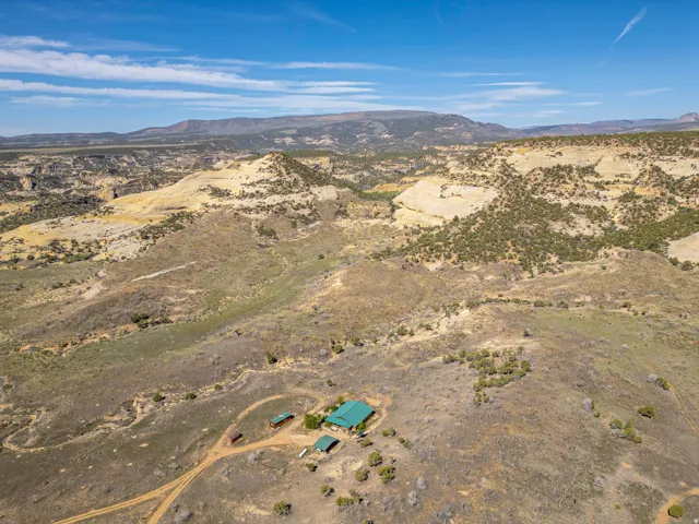 Expansive rural property featuring a main residence with a green roof, multiple outbuildings, and a dirt road entrance