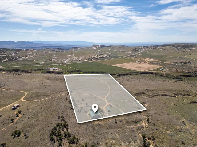 Expansive undeveloped land featuring a distinct property boundary, a single-story structure with a dark roof, and a winding dirt path