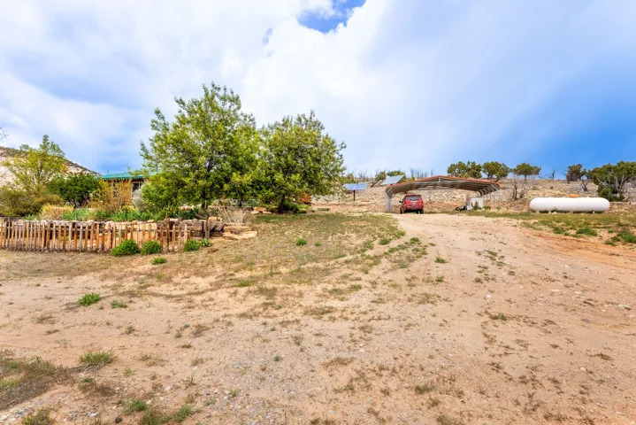 Gravel driveway leading to a stone carport and a separate propane tank