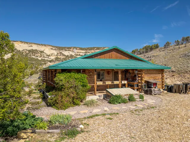 Log cabin exterior featuring a green metal roof, a covered porch, natural wood siding, and surrounding landscape with stone pathways