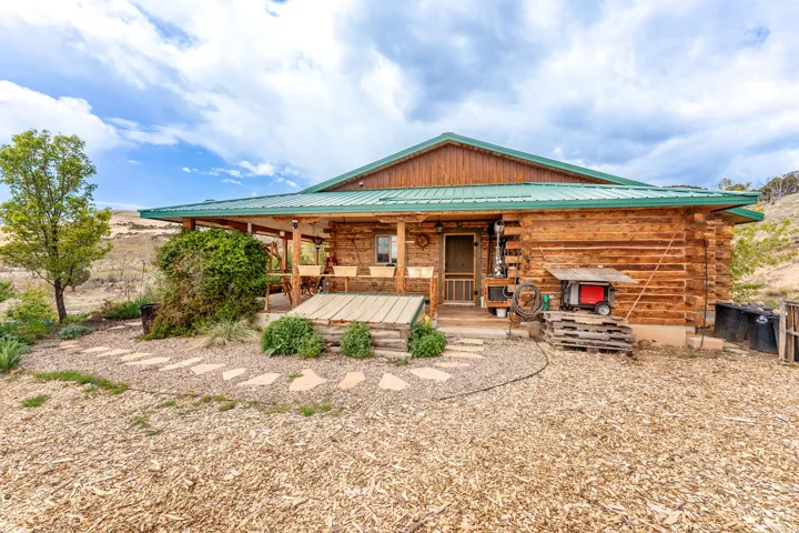 Log cabin exterior with a green metal roof, covered front porch, and a stone pathway