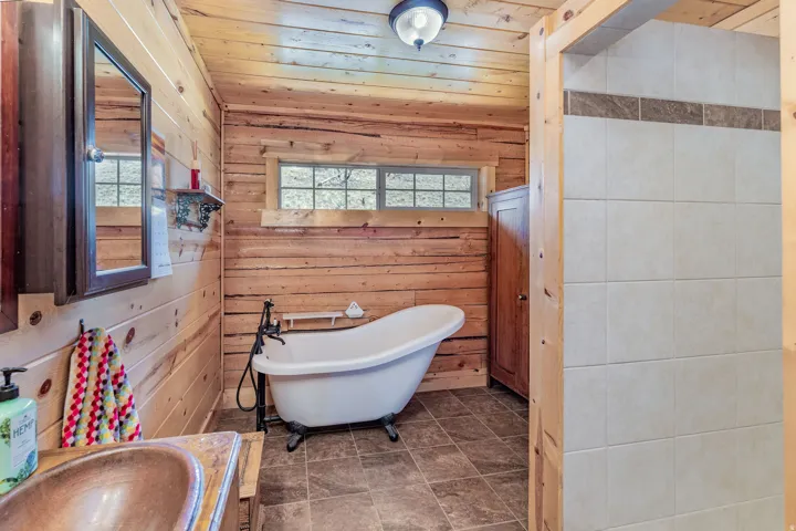 Bathroom featuring natural wood plank walls, a freestanding clawfoot bathtub with a vintage-style faucet, and a separate tiled shower enclosure