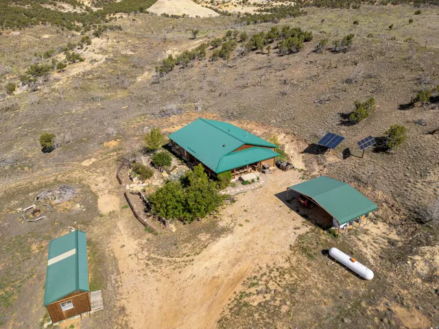 Main residence with green metal roofing, detached carport, separate outbuilding, and solar panel arrays