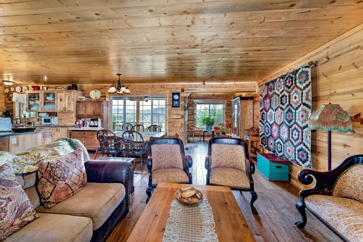 Spacious living area featuring extensive wood-finish paneling on walls and ceiling, wood-finish flooring, a built-in kitchen cabinetry with glass-front uppers, and large windows providing abundant natural light