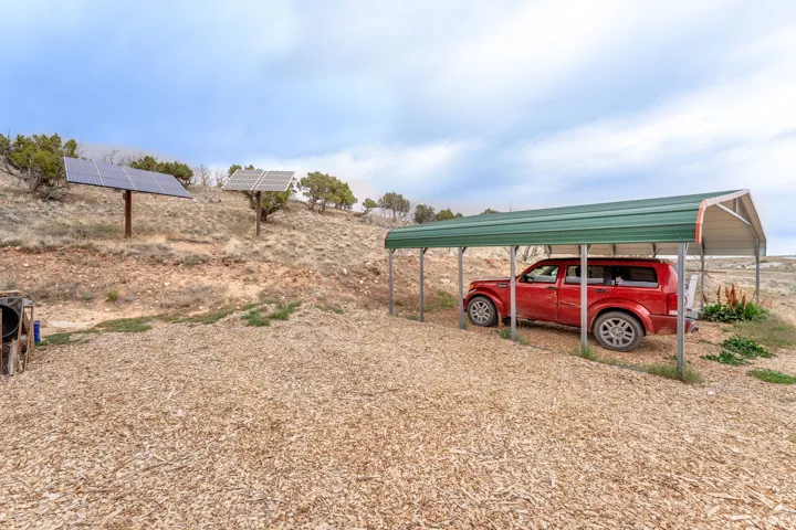 Expansive gravel and wood chip ground cover featuring a freestanding metal carport and two mounted solar panel arrays