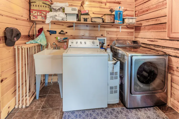 Utility space featuring wood paneling, a white utility sink, and durable tile flooring