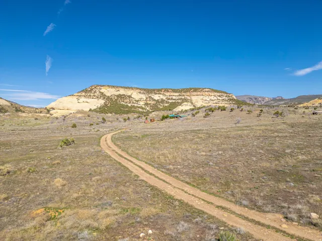Expansive open land featuring a winding dirt road, distant structures, and a prominent mesa backdrop