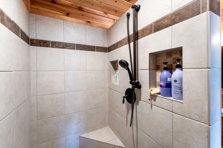 Tiled shower enclosure featuring a corner bench, a built-in niche, and a dark bronze shower fixture