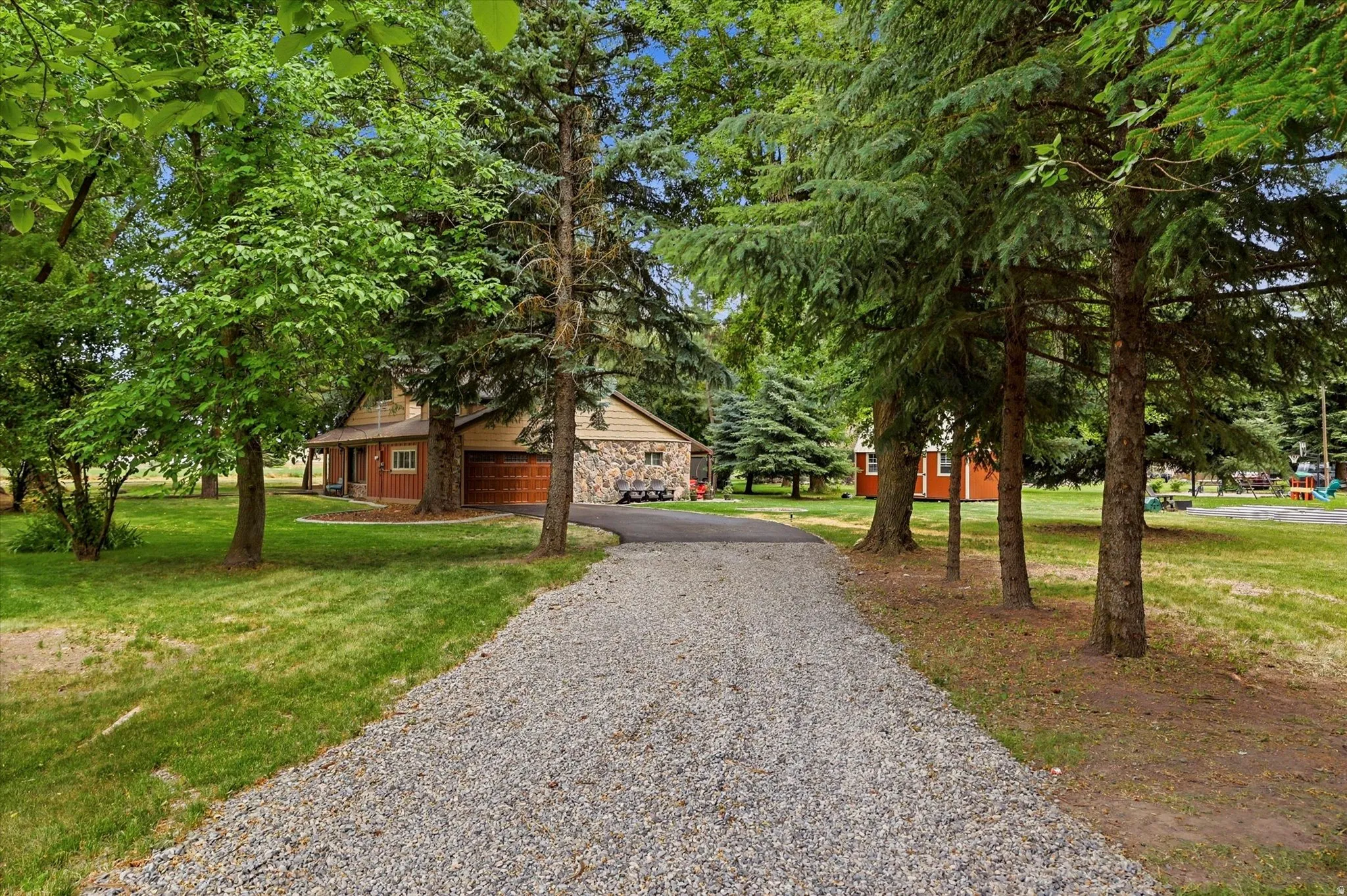 Gravel driveway leading to a residence featuring a wood-panel garage door, brick siding, and stone accents