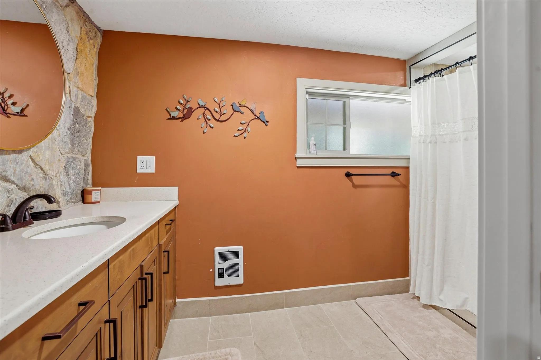 Bathroom featuring a built-in wood vanity with a white countertop and integrated sink, stone accent wall, and a full shower with a white curtain