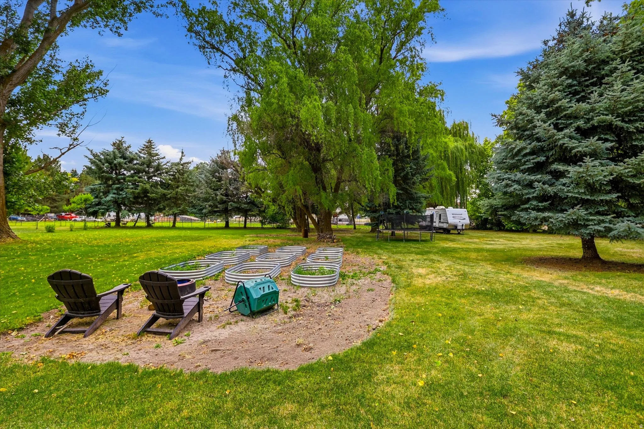 Spacious backyard featuring multiple raised garden beds, mature trees, and a manicured lawn