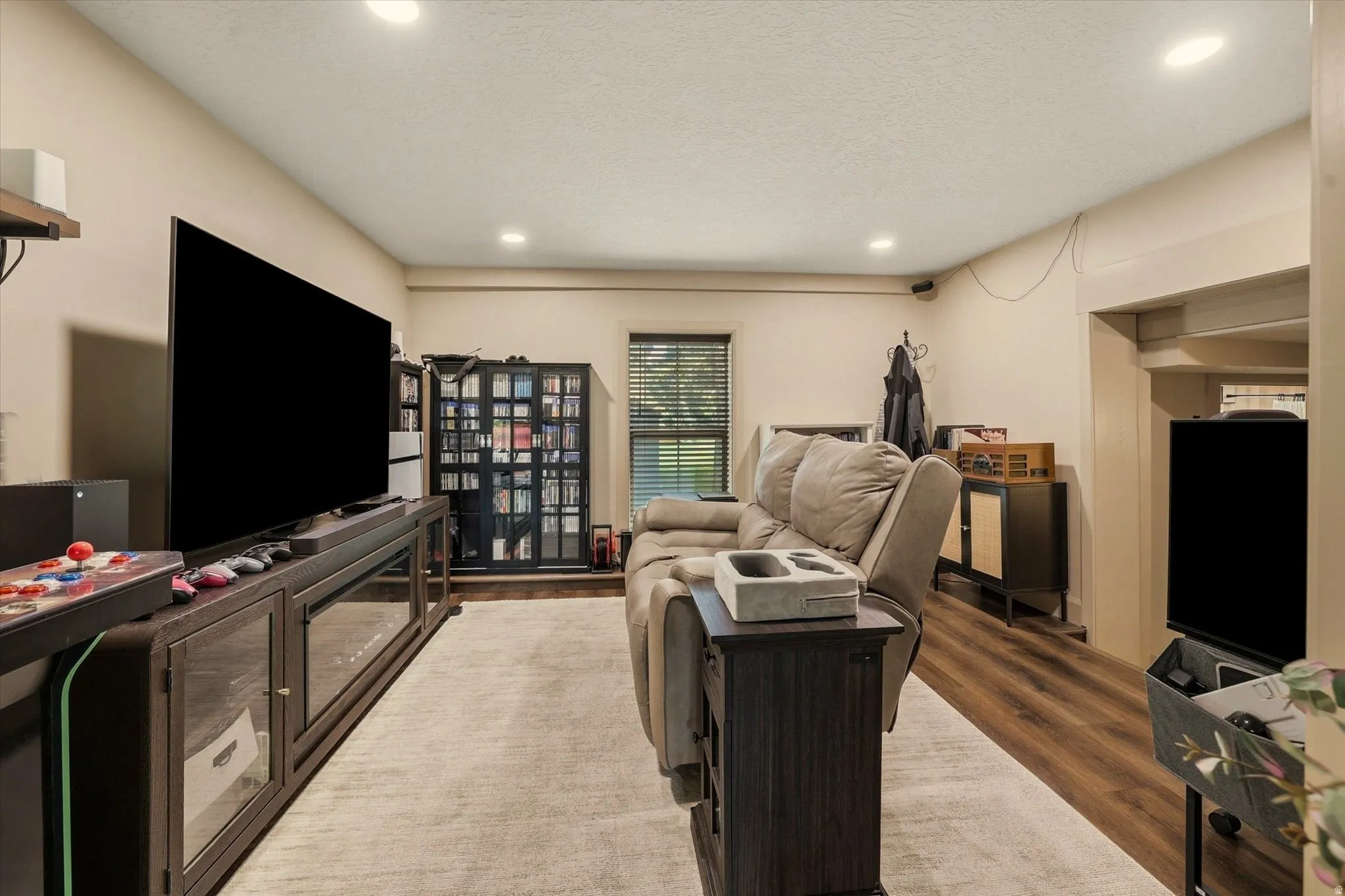 Living area featuring recessed lighting, a window with blinds, wood-finish flooring, and a wide cased opening