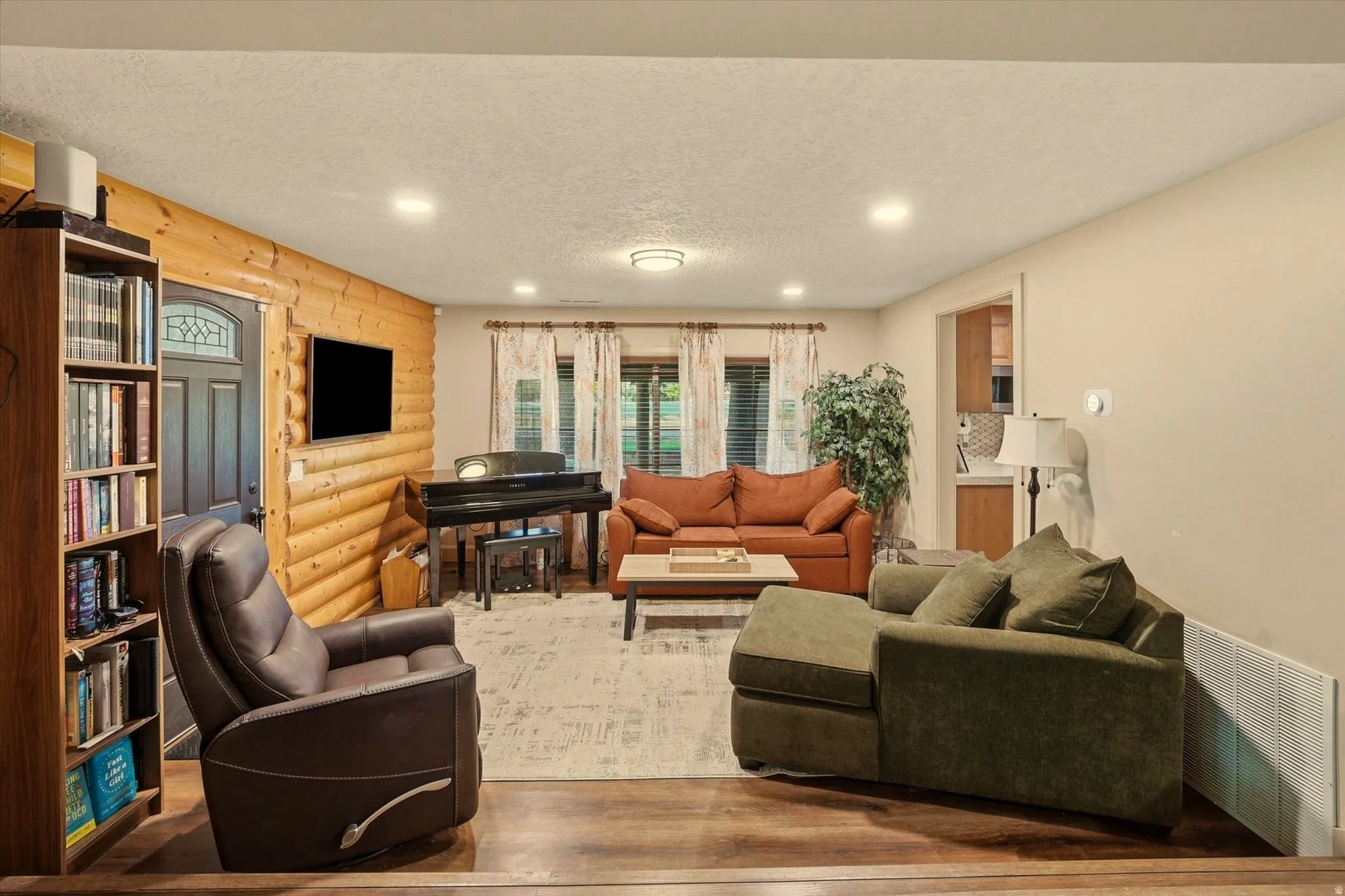 Living area featuring a log accent wall, wood-finish flooring, recessed lighting, and a dark wood entry door with decorative glass