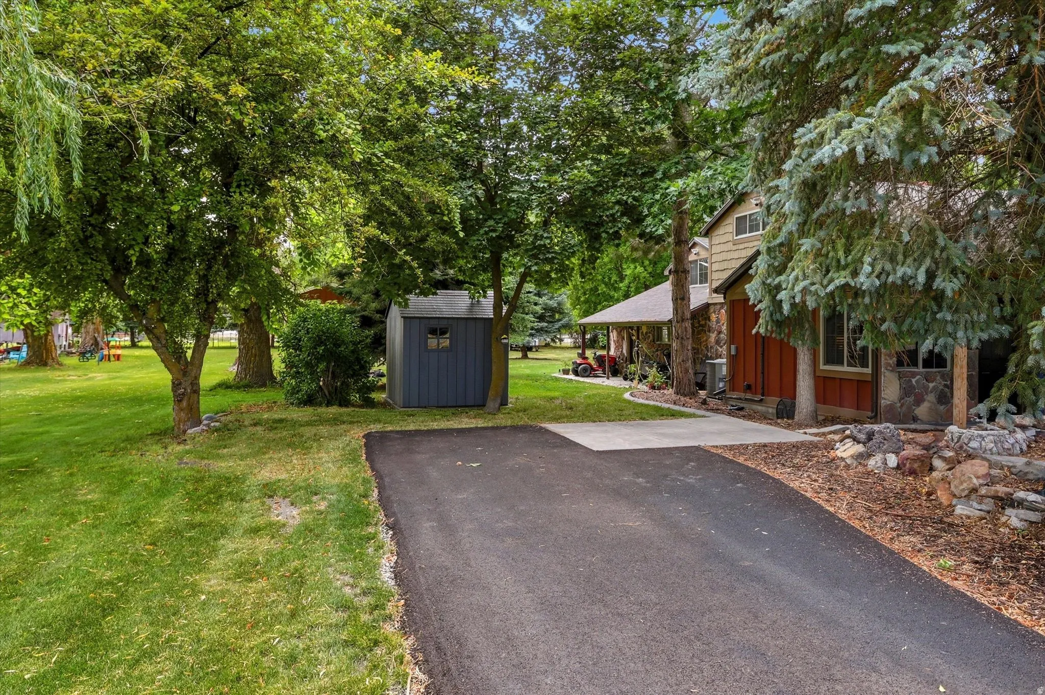 Expansive green lawn with mature trees, a paved driveway, and a detached storage shed
