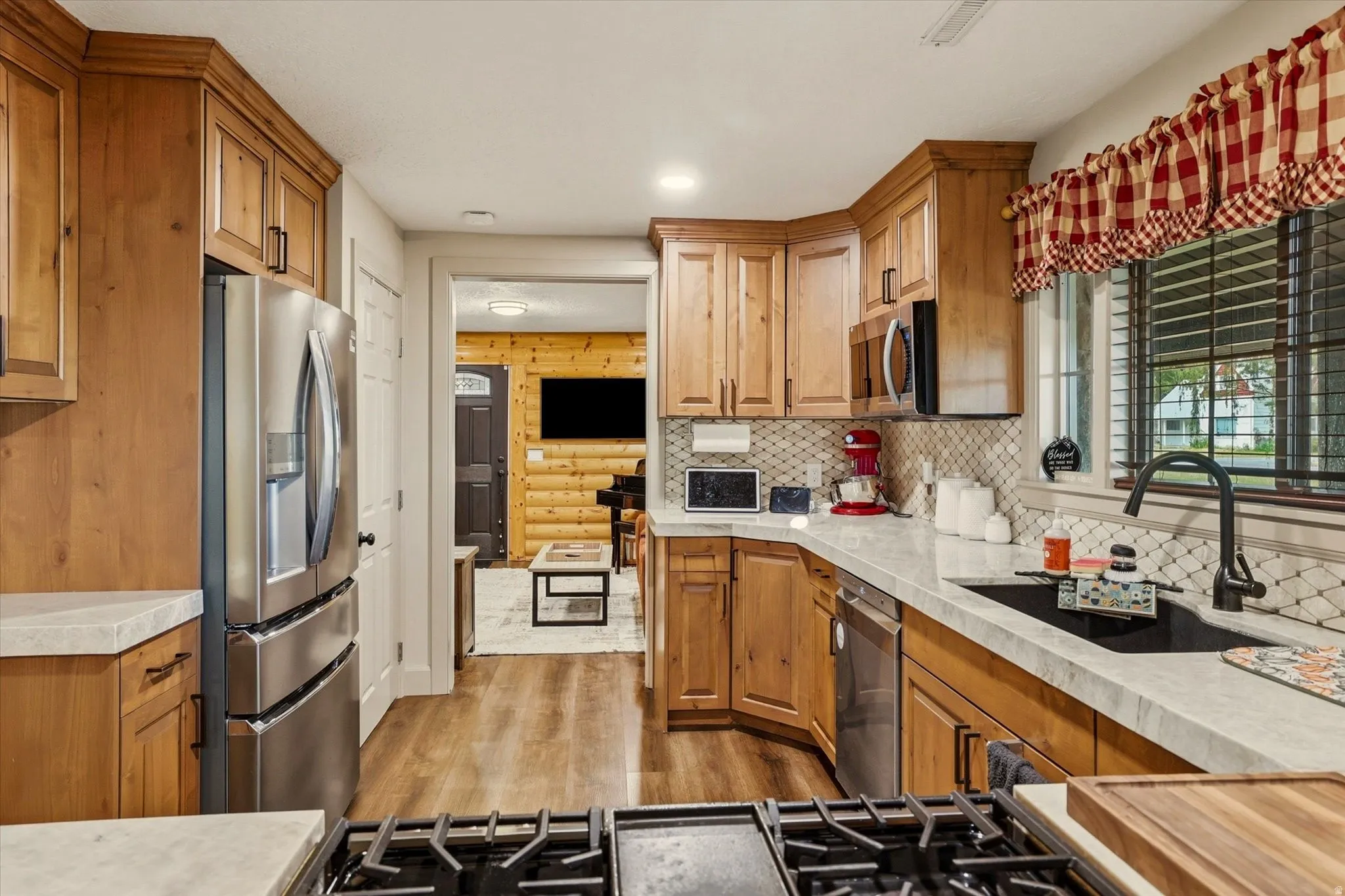 Kitchen featuring wood-finish cabinetry, stainless steel appliances, a gas range, light-toned countertops, and a patterned tile backsplash