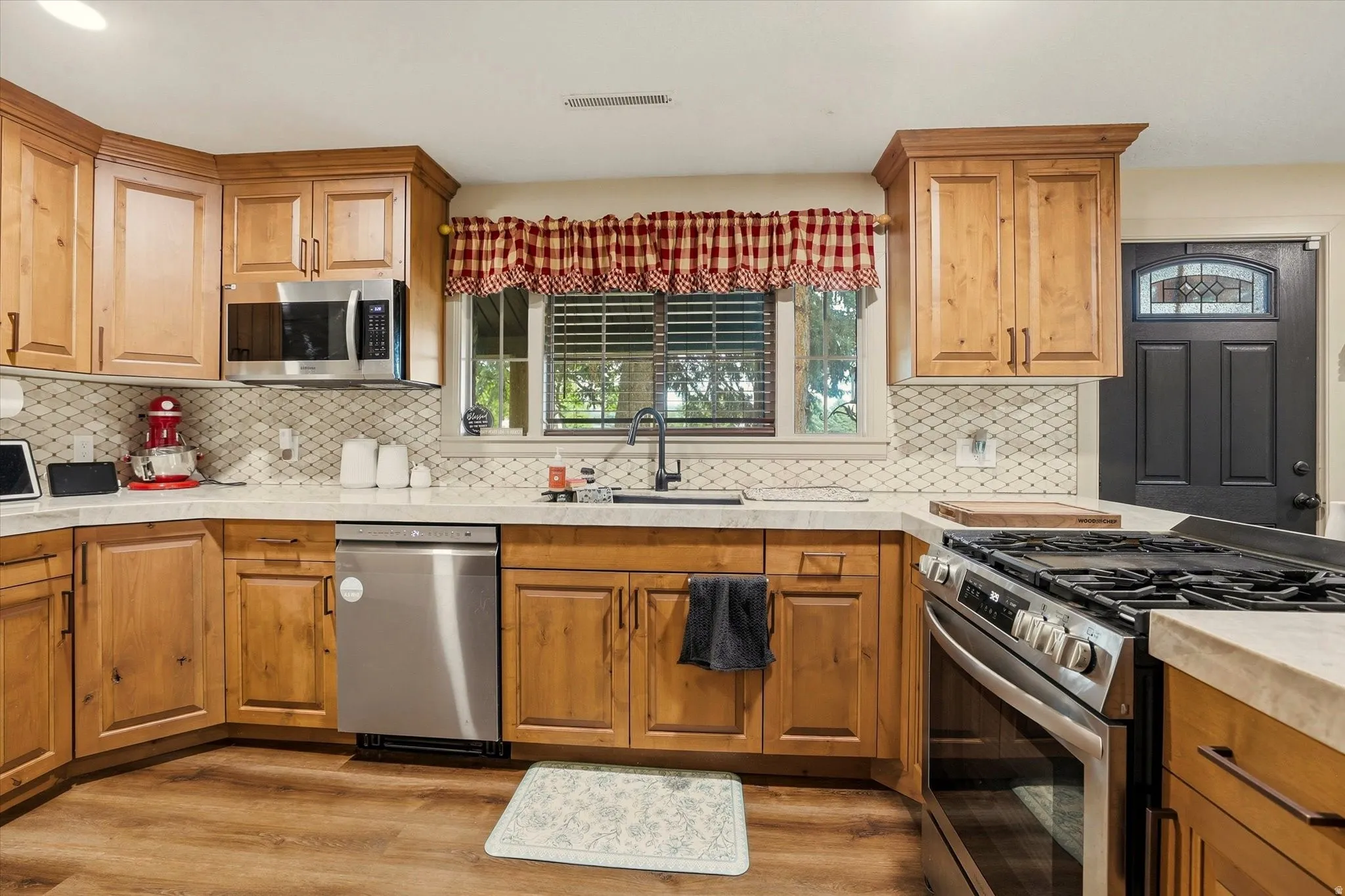 Kitchen featuring wood-finish cabinetry, light-toned countertops, and a full suite of stainless steel appliances including a gas range and built-in microwave