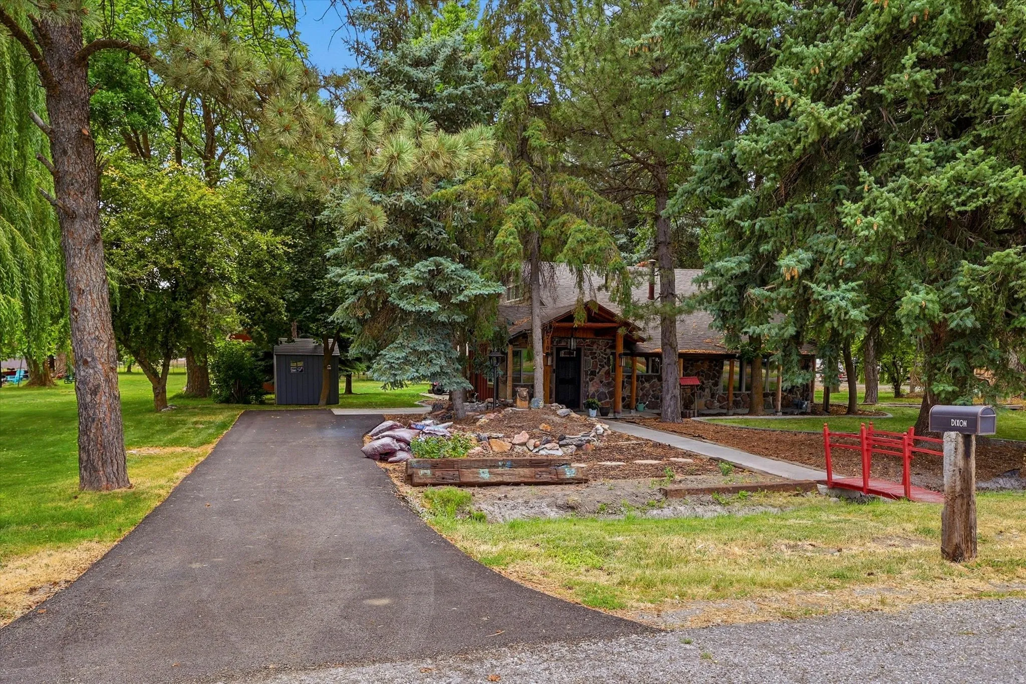 Paved driveway approaching a rustic-style residence with a stone facade and covered porch
