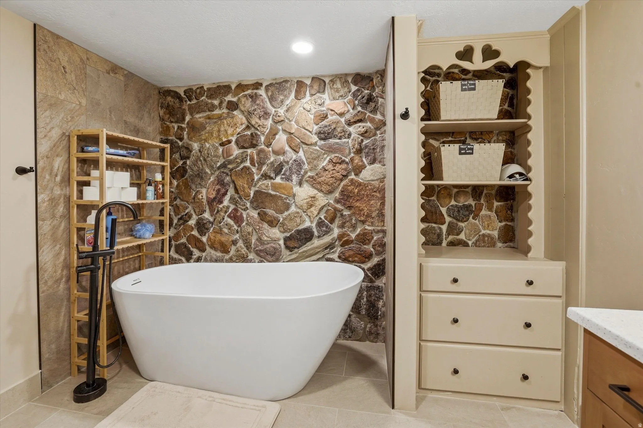 Freestanding soaking tub set against a natural stone accent wall, complemented by a floor-mounted matte black tub filler
