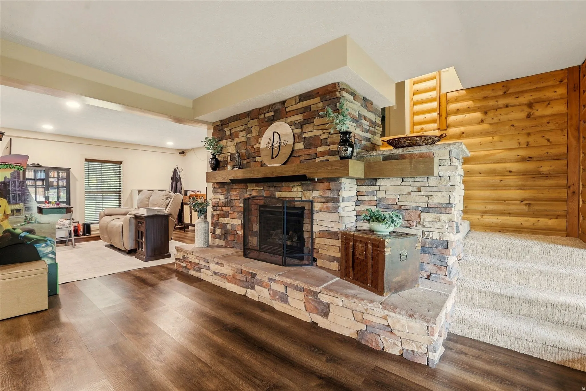 Stacked stone fireplace with a substantial hearth, wood-finish flooring, recessed lighting, and a carpeted staircase with wood paneling