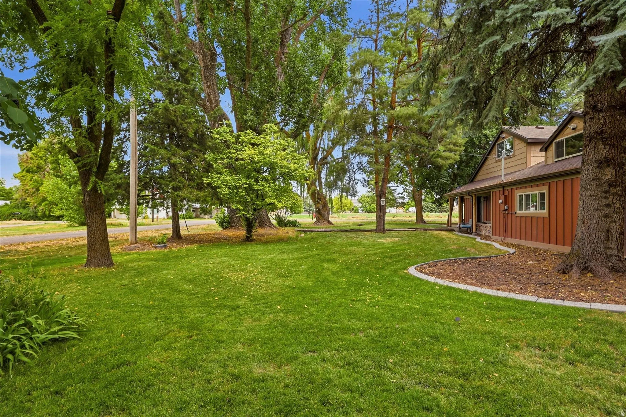 Expansive front yard featuring a manicured lawn, mature trees, and defined landscaping beds with stone curbing