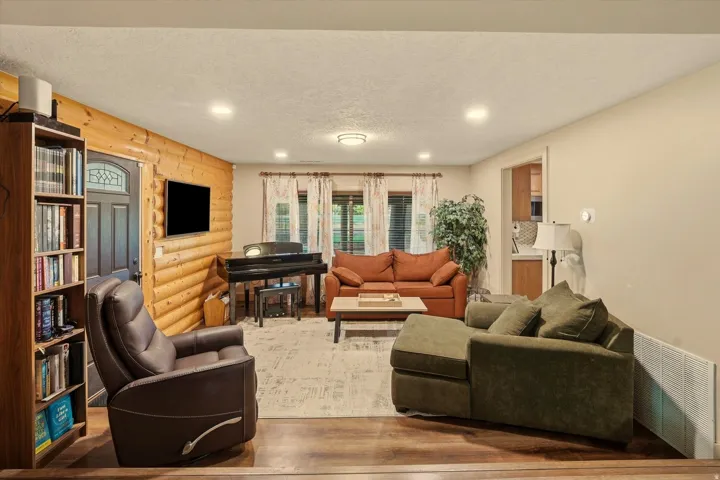 Living area featuring a log accent wall, wood-finish flooring, recessed lighting, and a dark wood entry door with decorative glass