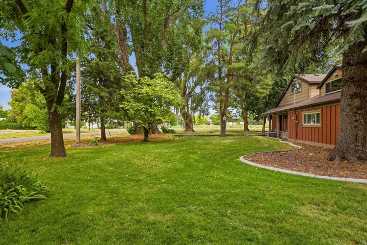 Expansive front yard featuring a manicured lawn, mature trees, and defined landscaping beds with stone curbing