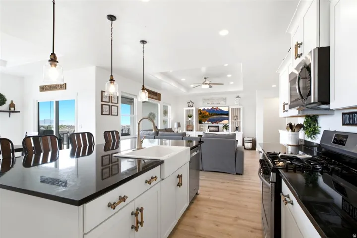 Open-concept kitchen featuring an island with a farmhouse sink, pendant lighting, white cabinetry with bronze hardware, and black countertops