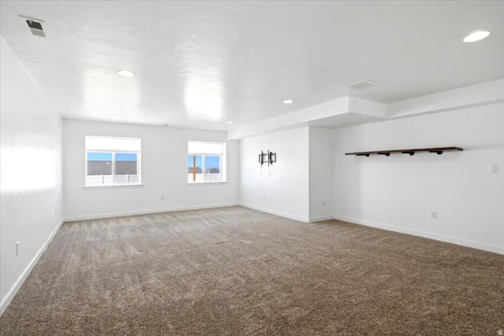 Spacious room featuring carpeting, two windows with blinds, recessed ceiling lighting, and a wall-mounted shelf