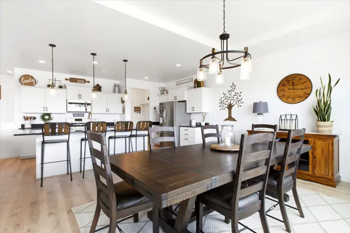 Open-concept dining area with a modern chandelier, light wood-finish flooring, and white walls